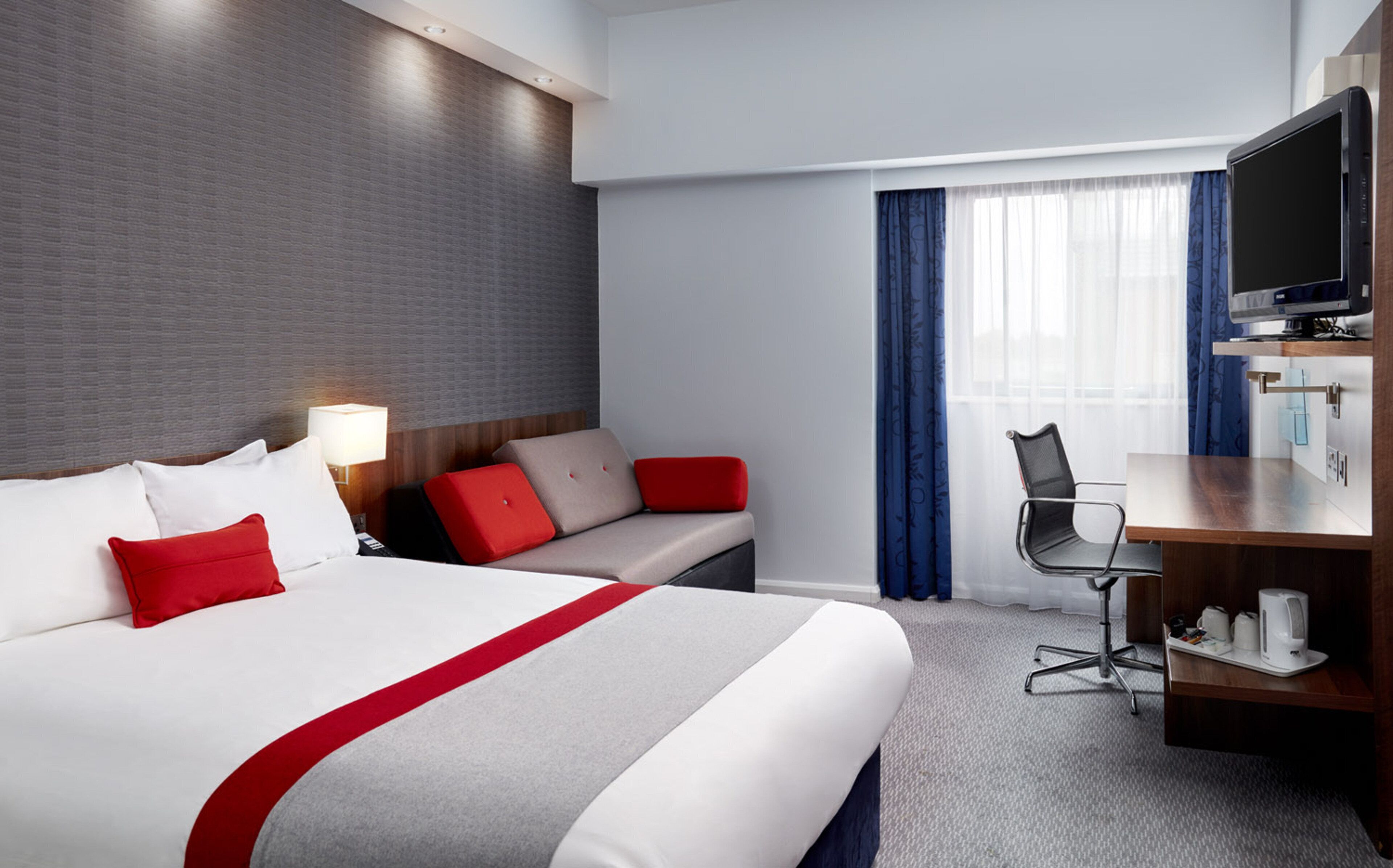 A hotel room with a bed, a desk, a chair, a television, and a window with curtains.