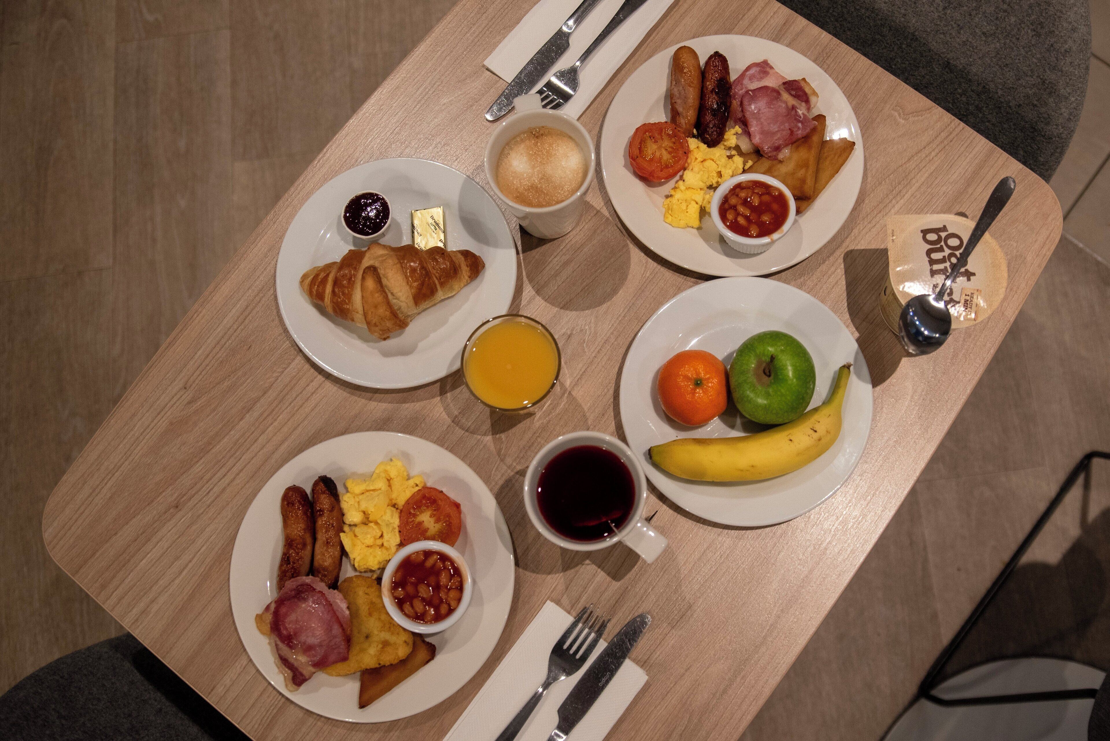 A breakfast table with plates of eggs, sausages, ham, toast, and fruit.