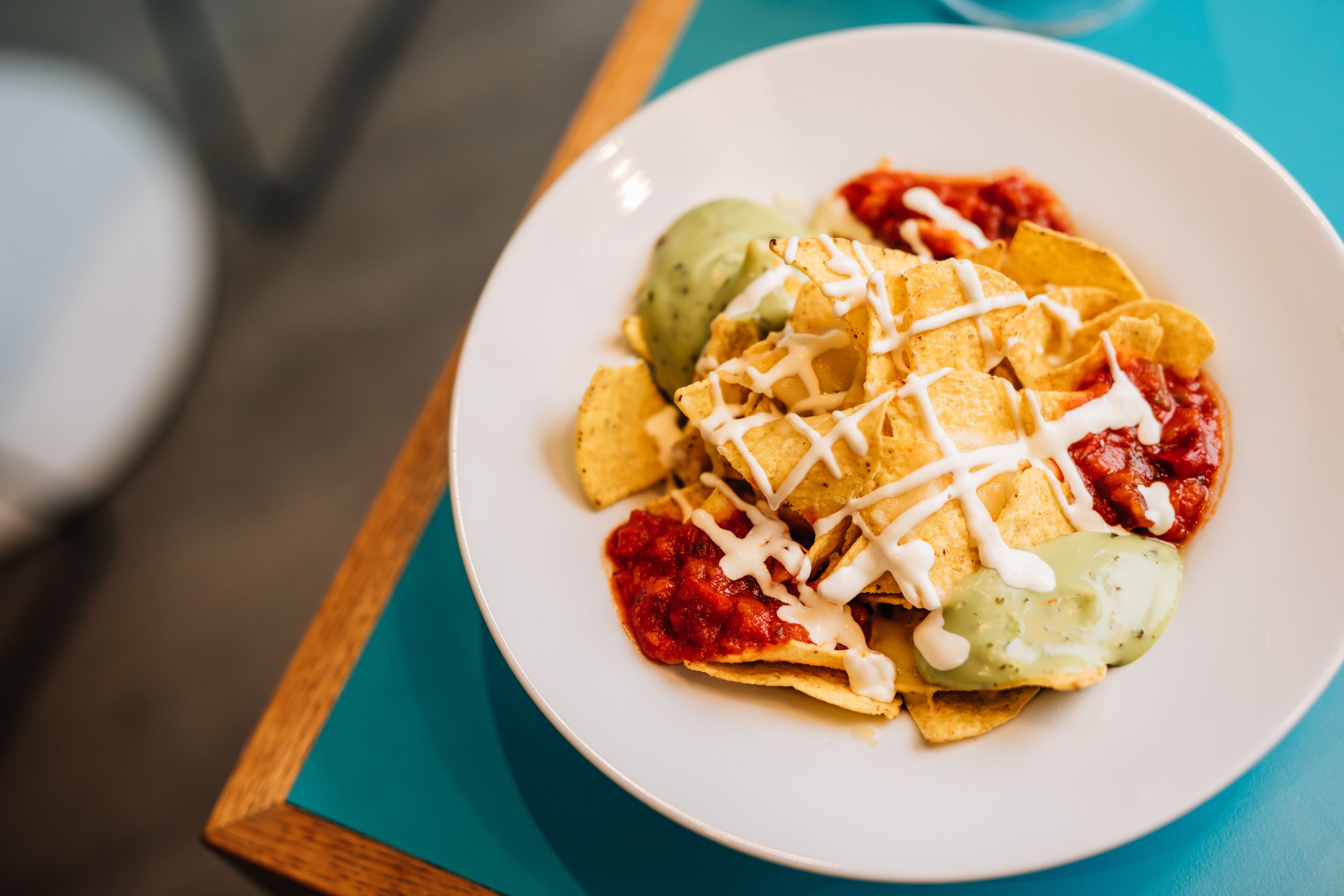 Eine Portion Nachos mit Guacamole und einer weißen Soße auf einem türkisfarbenen Tisch.