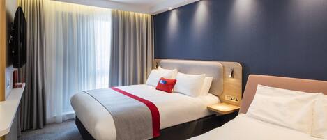 A hotel room with a large bed, a bedside table, a TV, and a window with curtains.