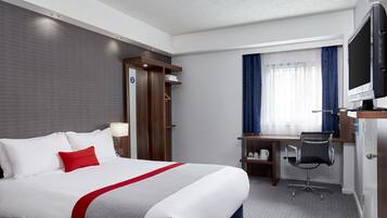 Une chambre d’hôtel avec un lit, un bureau, une chaise, une télévision et une fenêtre avec des rideaux.