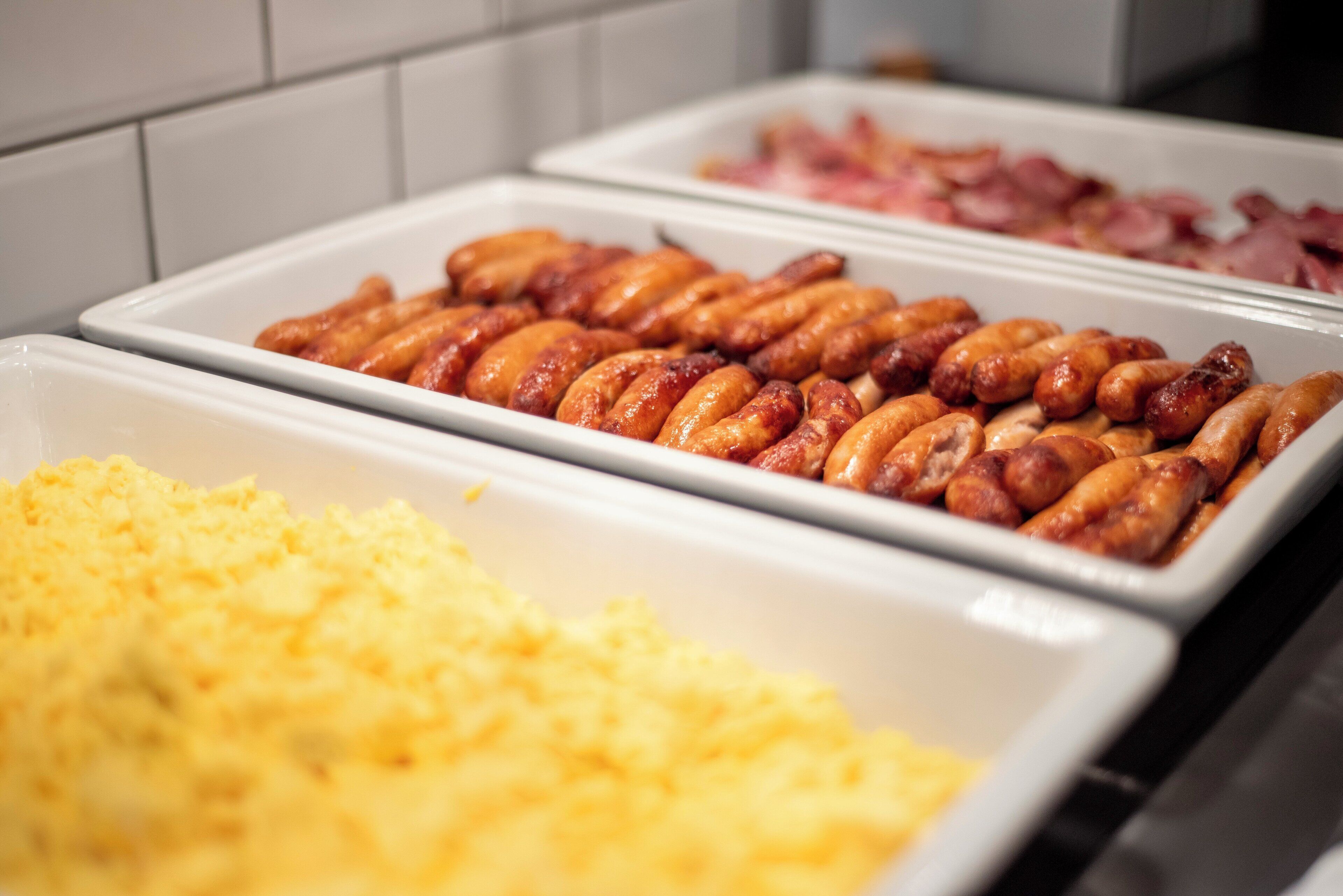 A buffet with trays of food including sausages, ham, and scrambled eggs.