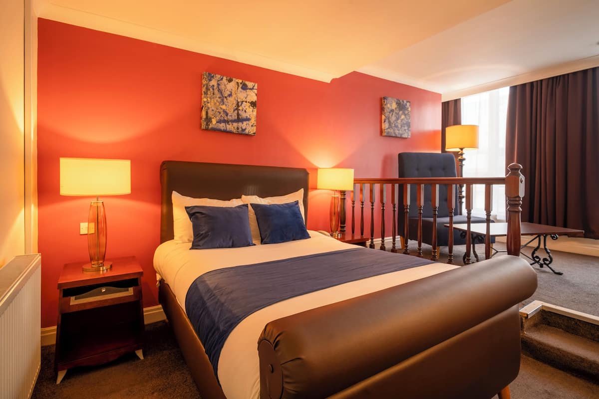 A hotel room with a large bed, two bedside tables with lamps, a chair, and artwork on the walls.