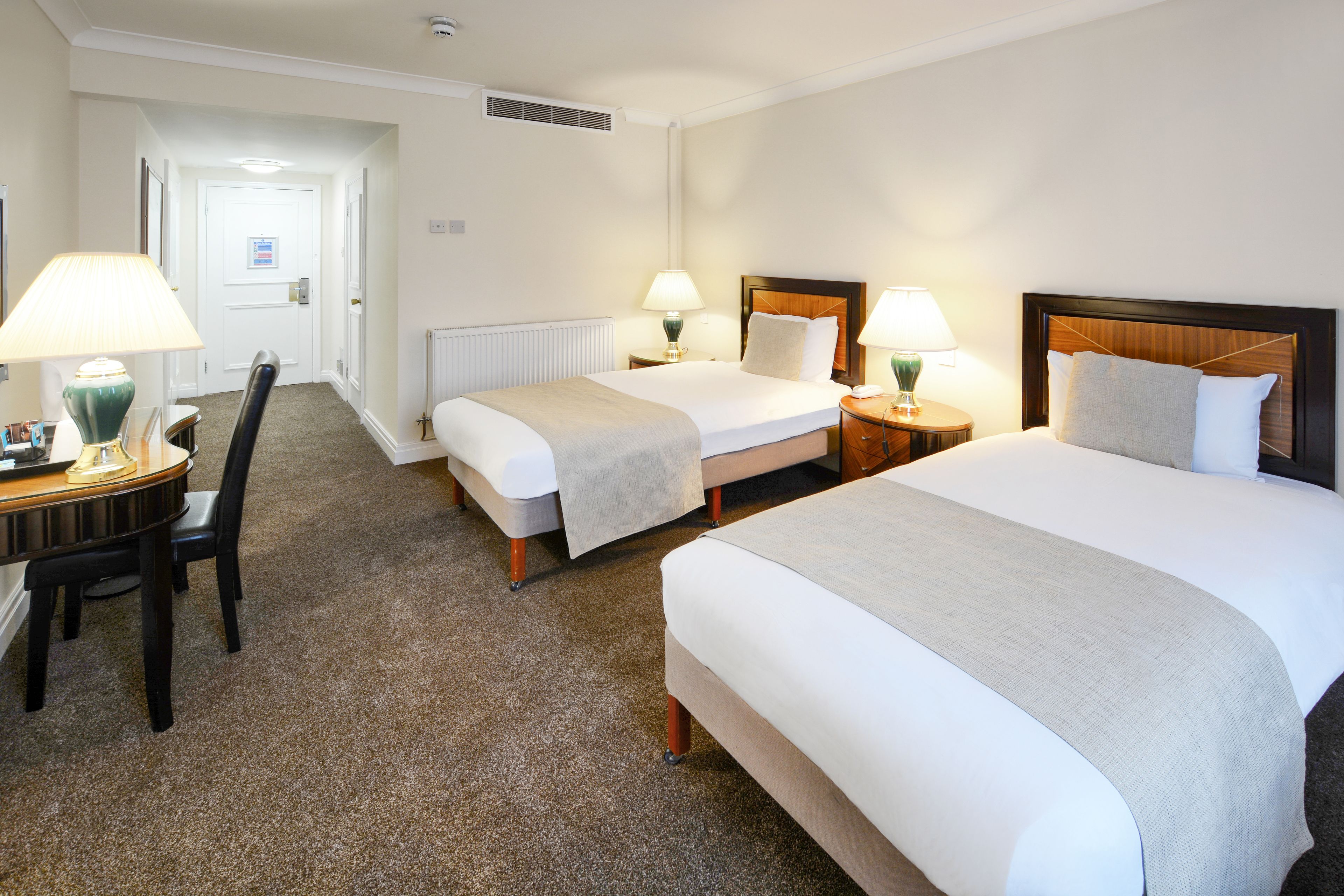 A hotel room with two single beds, a desk with a chair, and two bedside lamps.