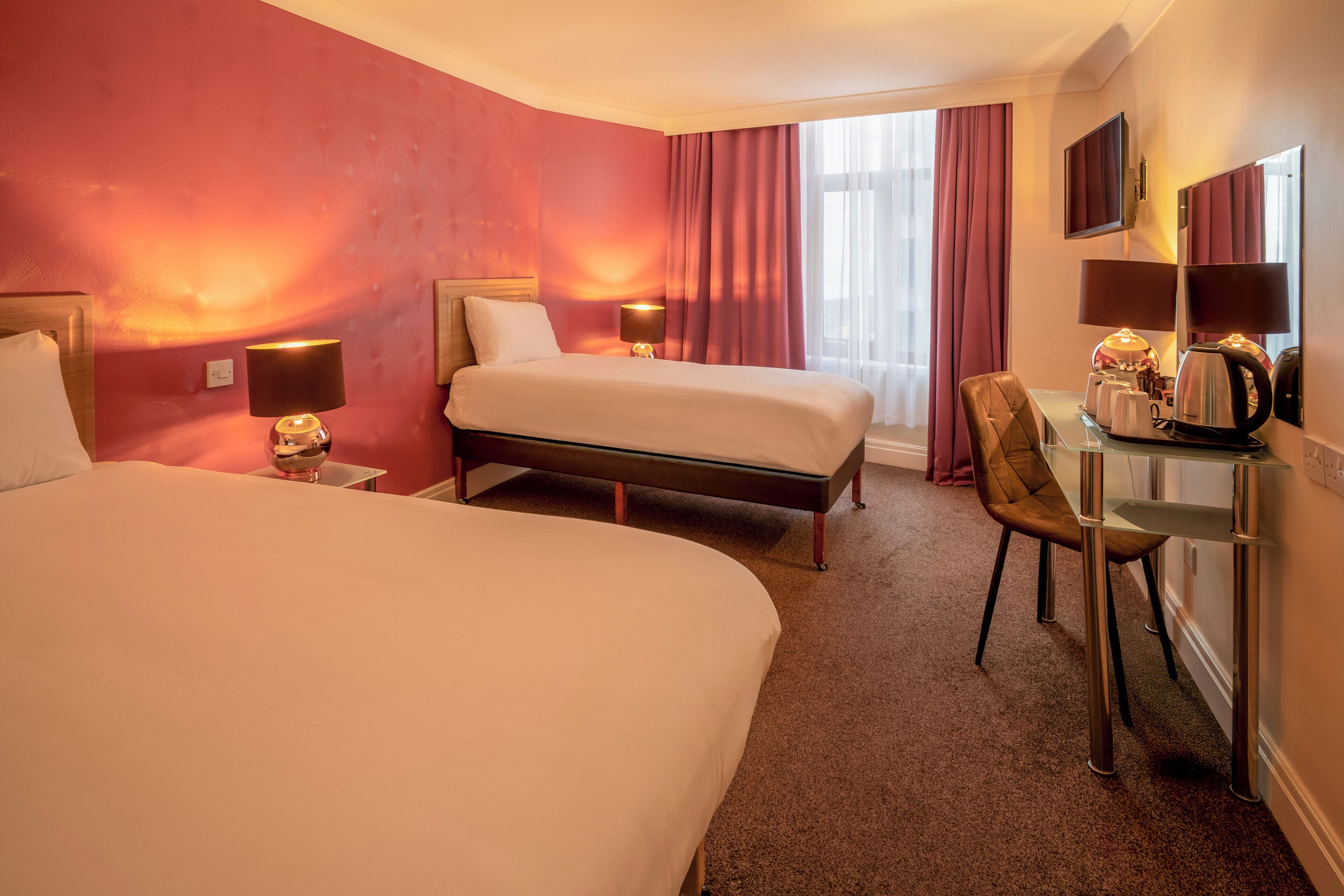 A hotel room with two beds, a desk with a chair, a television, and a window with curtains.