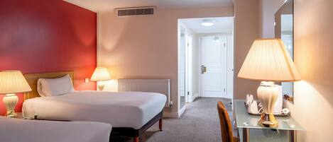A hotel room with two beds, a desk with a chair, and a mirror.