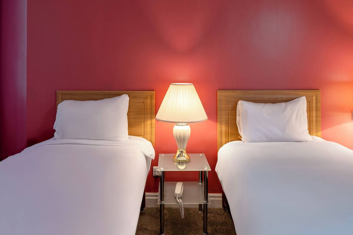 A hotel room with two beds, a bedside table with a lamp, and a telephone.