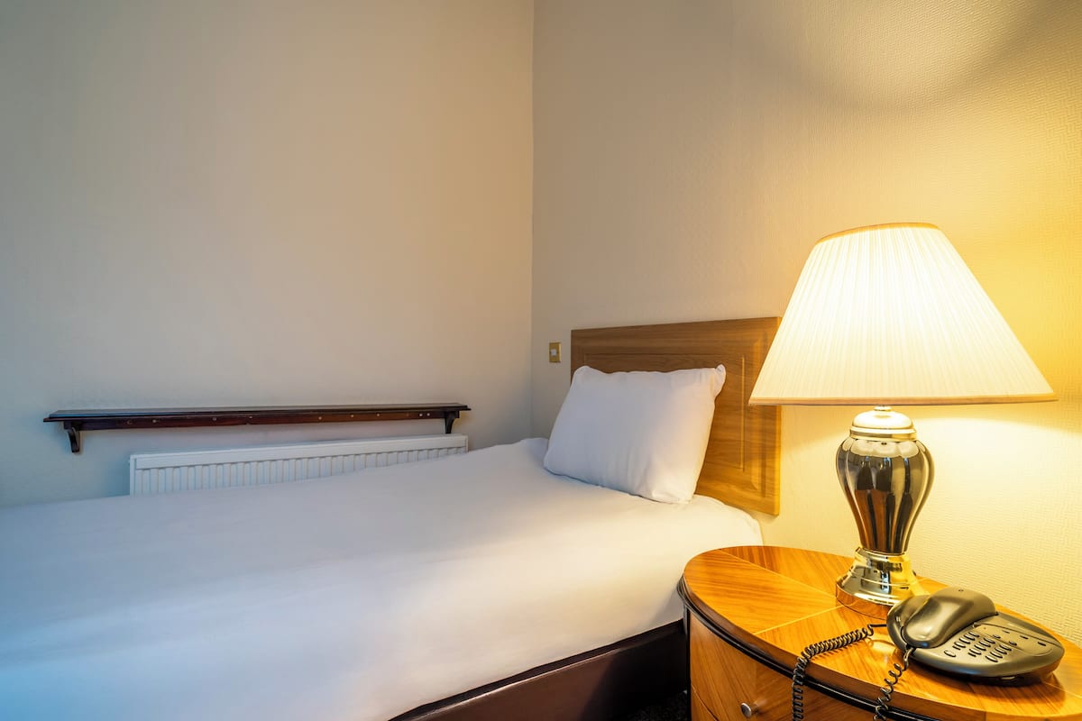 A hotel room with a bed, a bedside lamp, a telephone, and a wooden headboard.