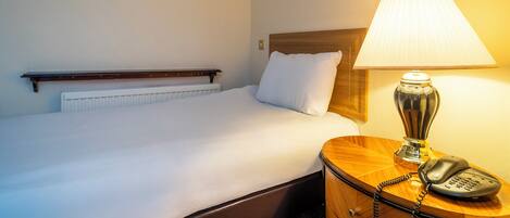 A neatly made bed with a wooden headboard, a bedside lamp, and a telephone on a wooden nightstand.
