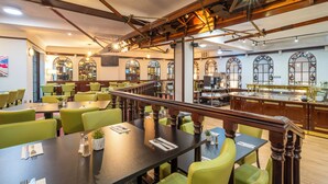 A restaurant with green chairs, wooden tables, and a bar area. - Britannia Sachas Hotel (Manchester)