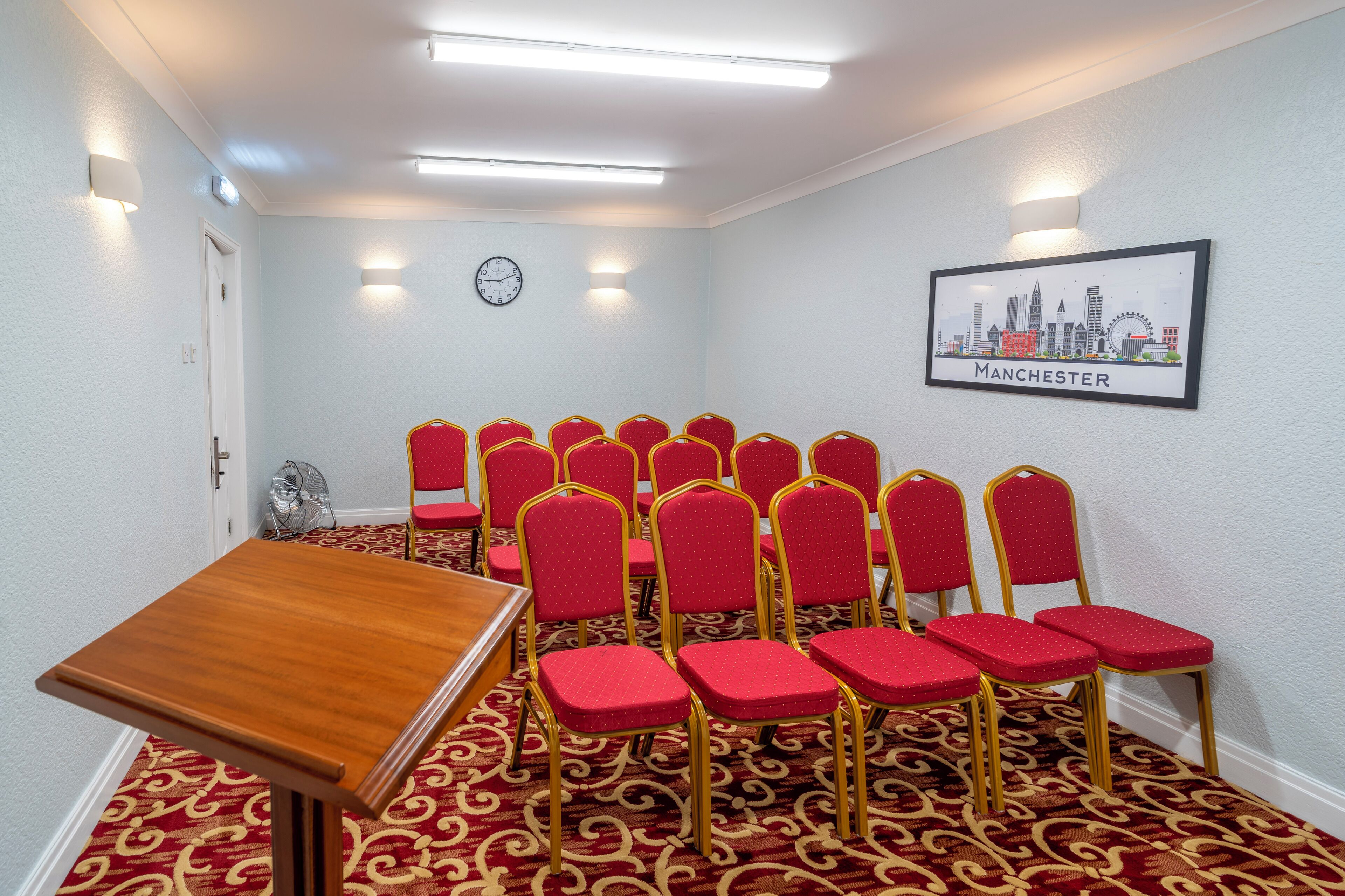 A conference room with a wooden table and red chairs, a clock, and a cityscape poster on the wall.