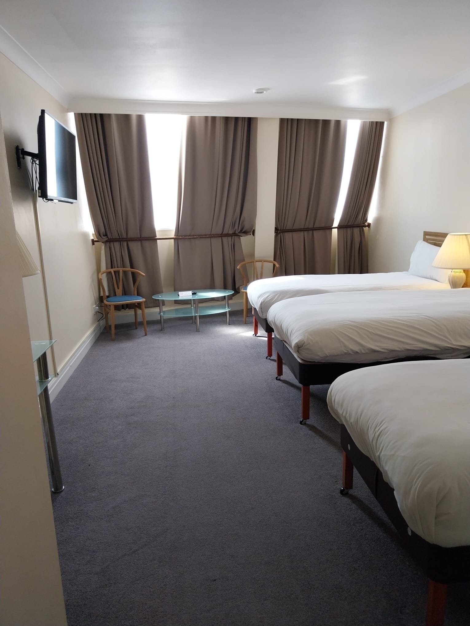 A hotel room with two beds, a desk, chairs, a TV, and a window with curtains.