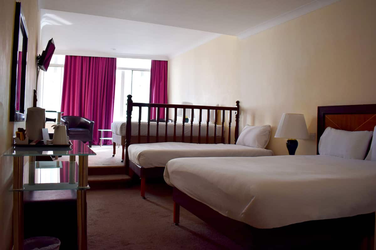 A hotel room with two single beds, a desk with a chair, a lamp, and a window with curtains.