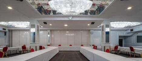A conference room with long tables, red chairs, a chandelier, and a large mirror on the ceiling.