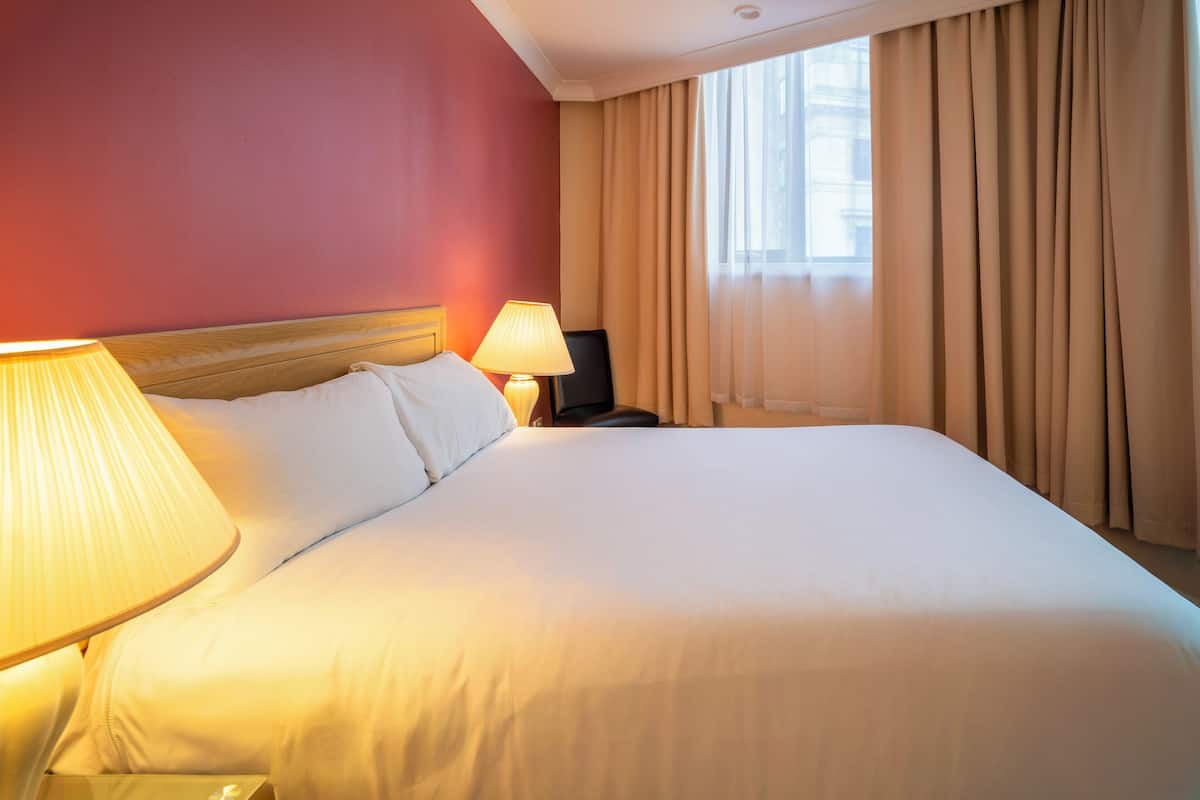 A hotel room with a large bed, a bedside lamp, a nightstand, and a window with curtains.