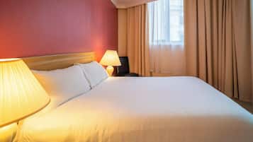A hotel room with a large bed, a bedside lamp, a nightstand, and a window with curtains.