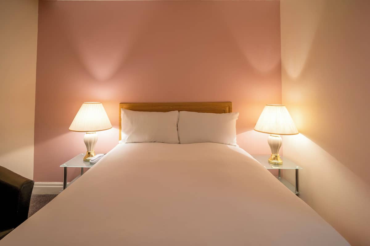 A neatly made bed with white linens and two bedside lamps on matching nightstands.