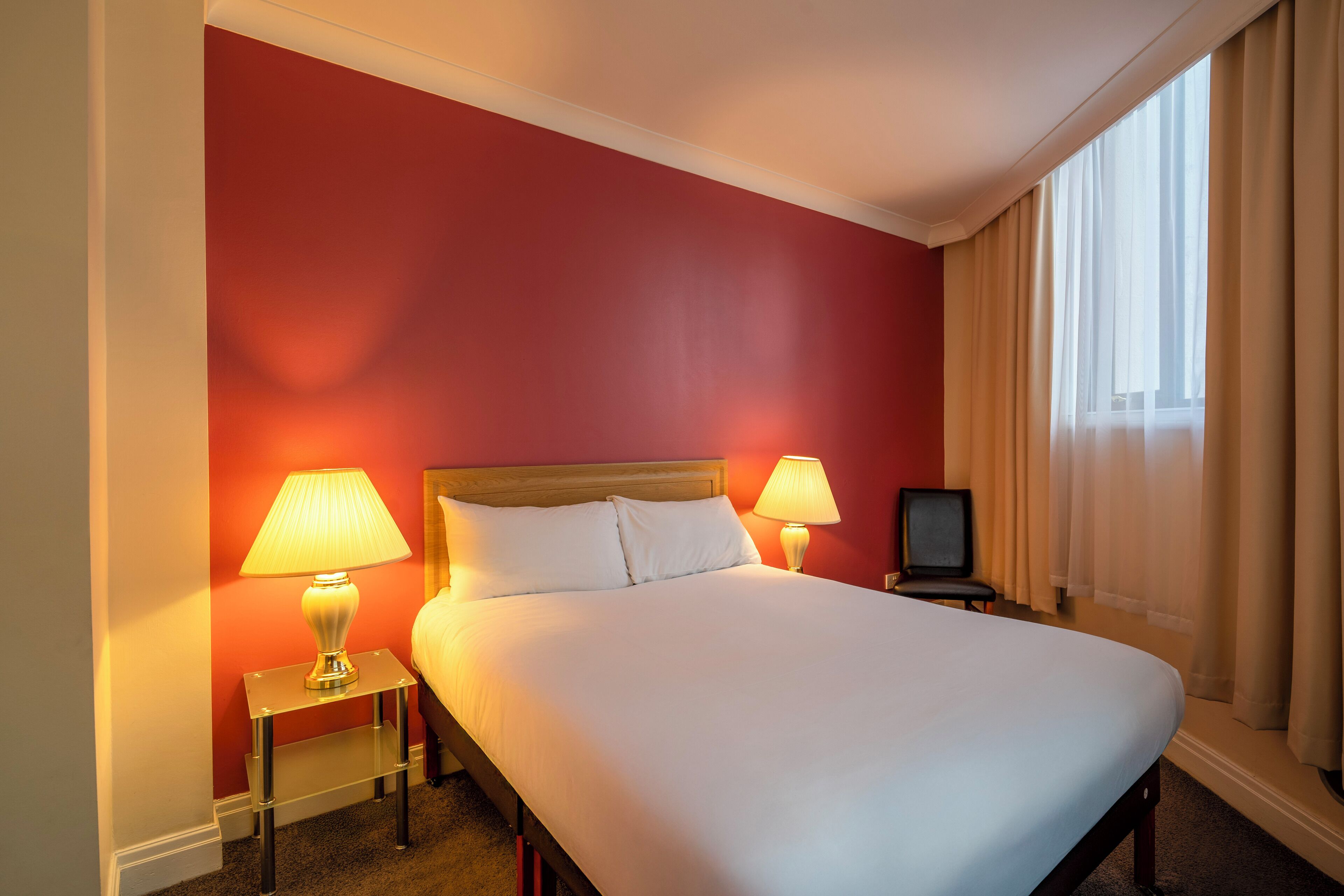A hotel room with a large bed, two bedside lamps, a television on a small table, and a window with curtains.
