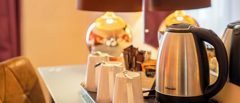 A tray with a stainless steel electric kettle and white cups on a glass table.