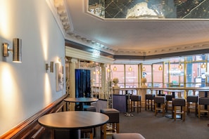 A bar area with round tables and bar stools, a decorative ceiling, and large windows with a view of the street. - Britannia Sachas Hotel (Manchester)