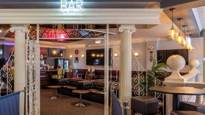 A bar area with a neon sign, seating, and a television screen. - Britannia Sachas Hotel (Manchester)