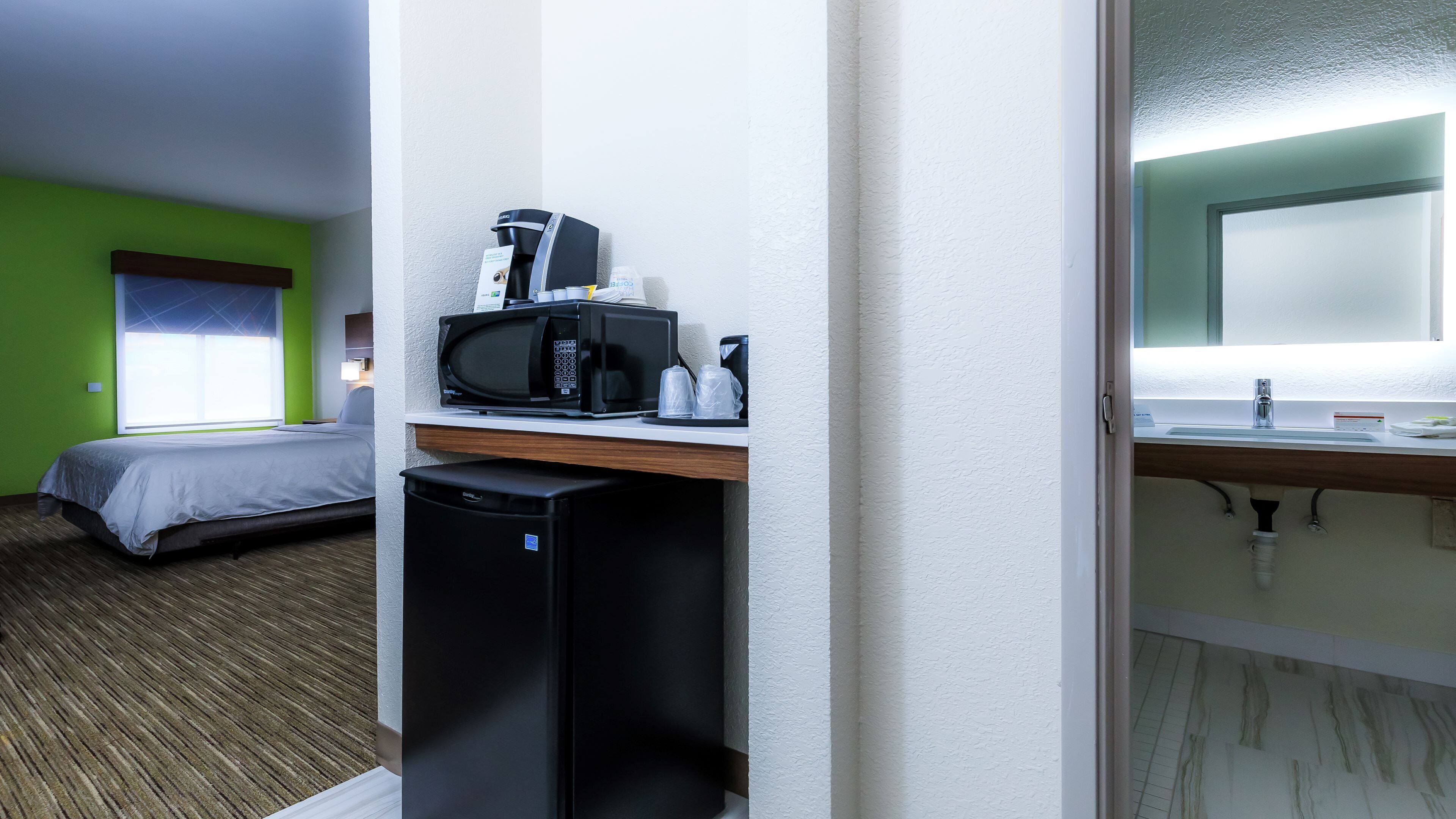 A hotel room with a bed, a microwave, a coffee maker, and a small refrigerator.