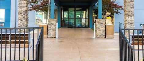A building entrance with a covered walkway, stone pillars, and a metal railing.