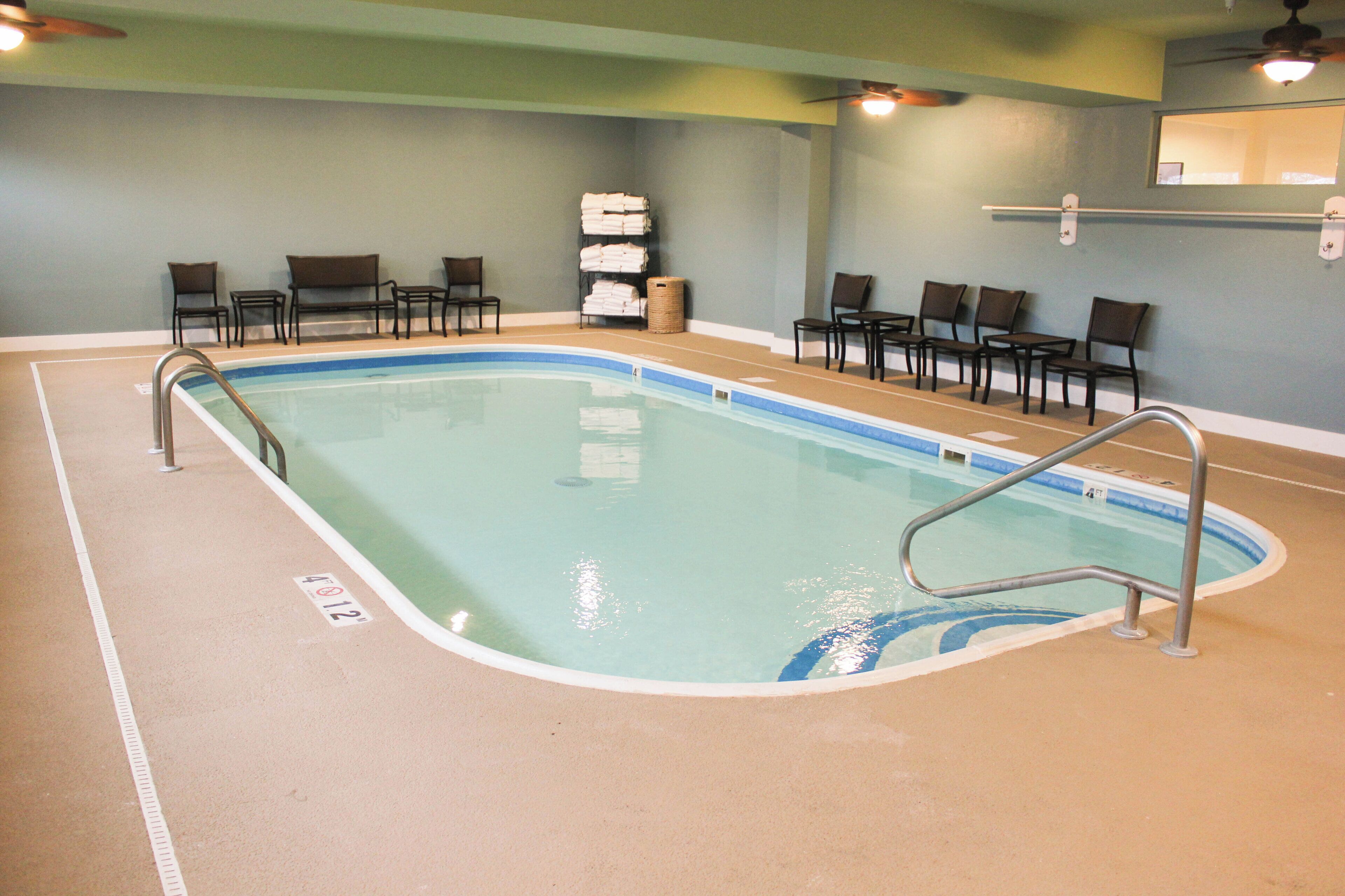 An indoor swimming pool with a clear waterline, surrounded by chairs and a bench.
