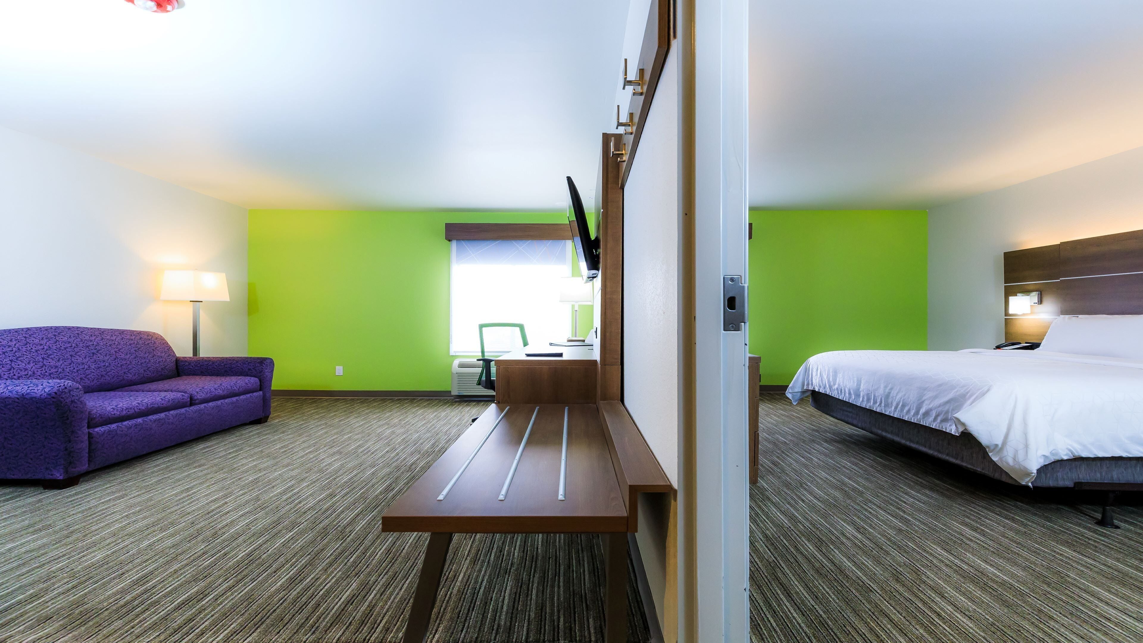A hotel room with a bed, a desk, a chair, a sofa, and a TV.
