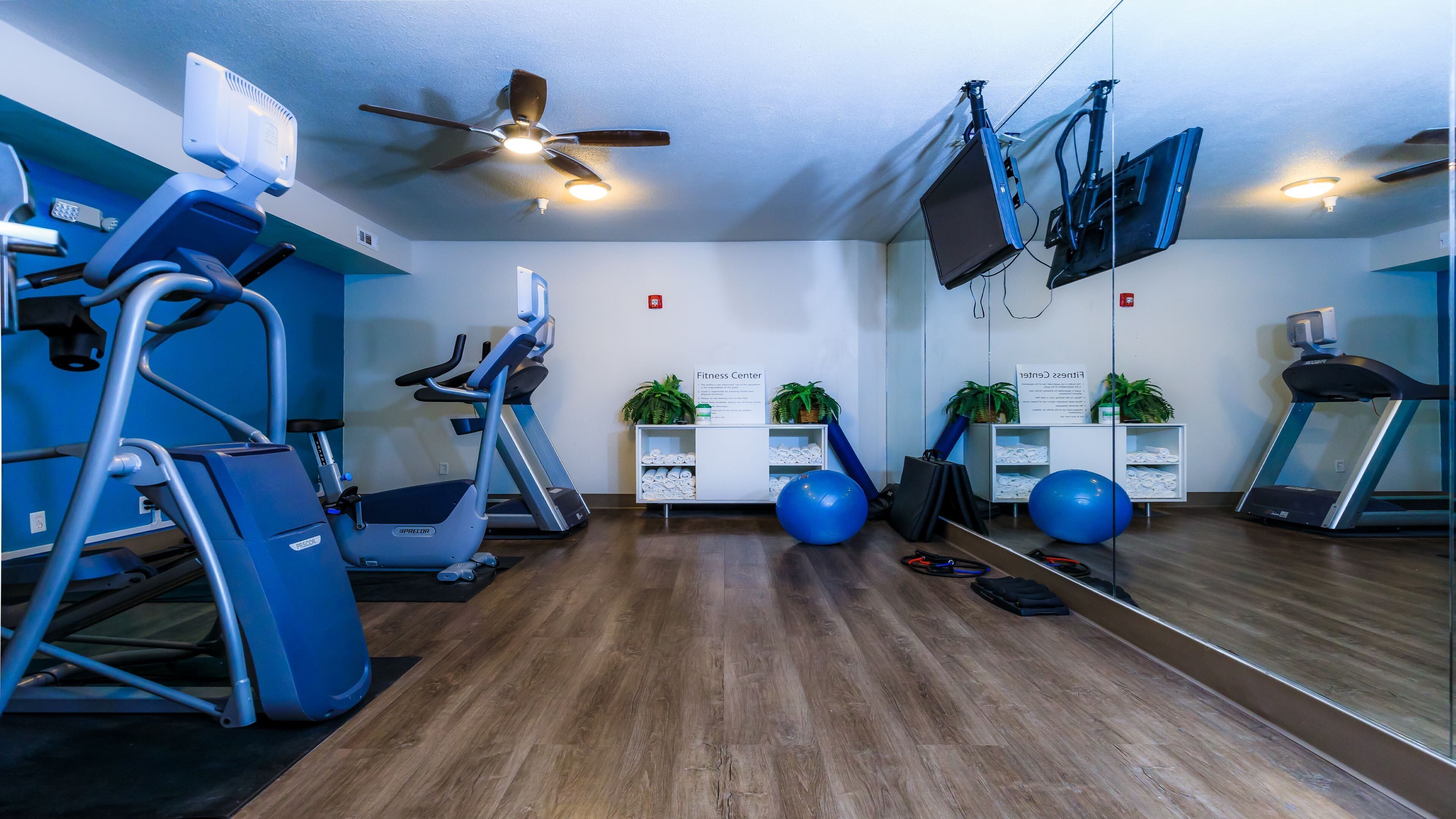 A fitness center with exercise equipment, a ceiling fan, and a sign indicating the space.