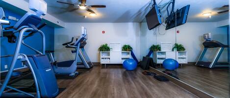A fitness center with exercise equipment, a ceiling fan, and a sign indicating the space.