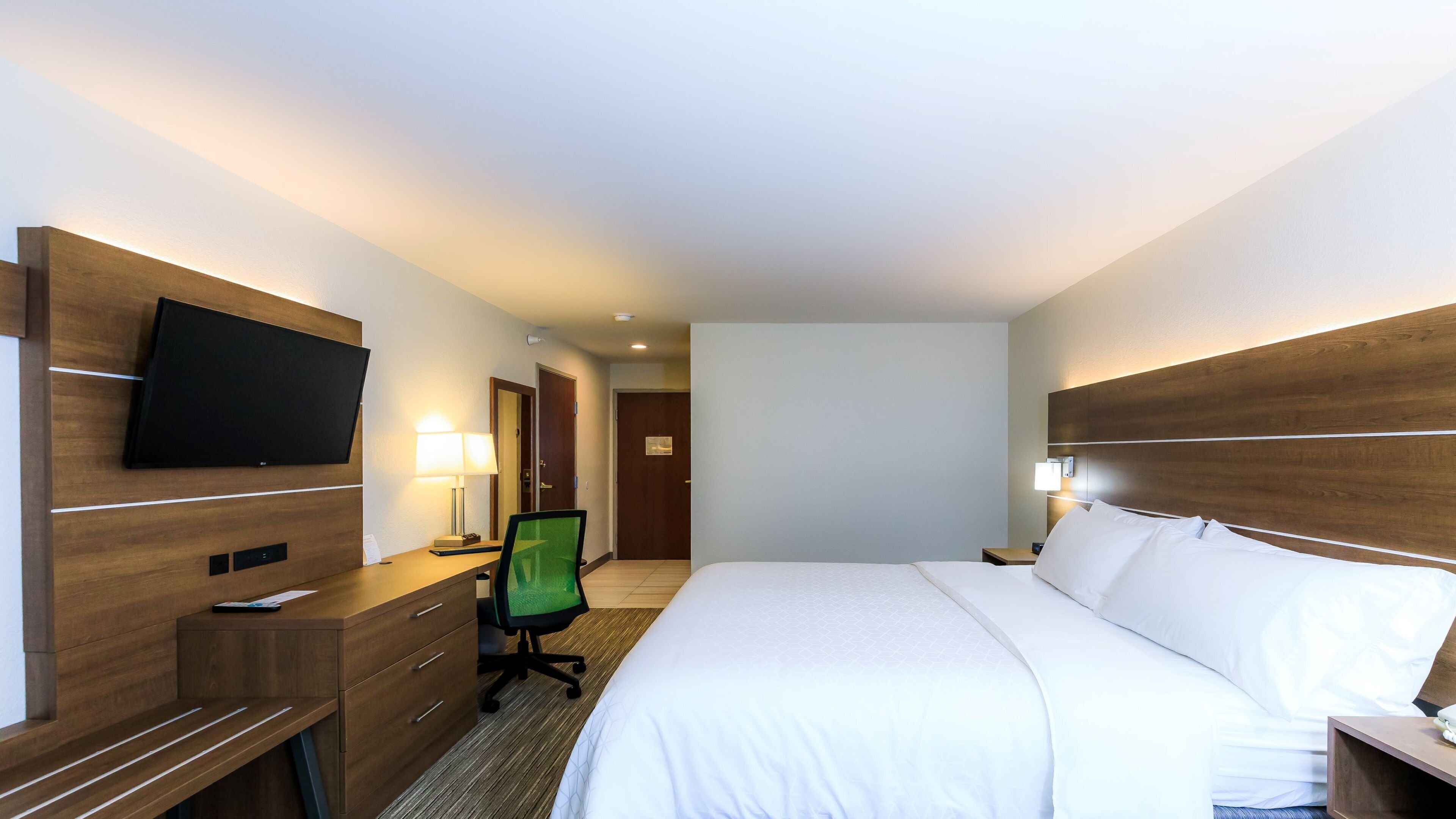 Ein Hotelzimmer mit einem Bett, einem Schreibtisch mit Stuhl, einem Fernseher und einem Nachttisch.