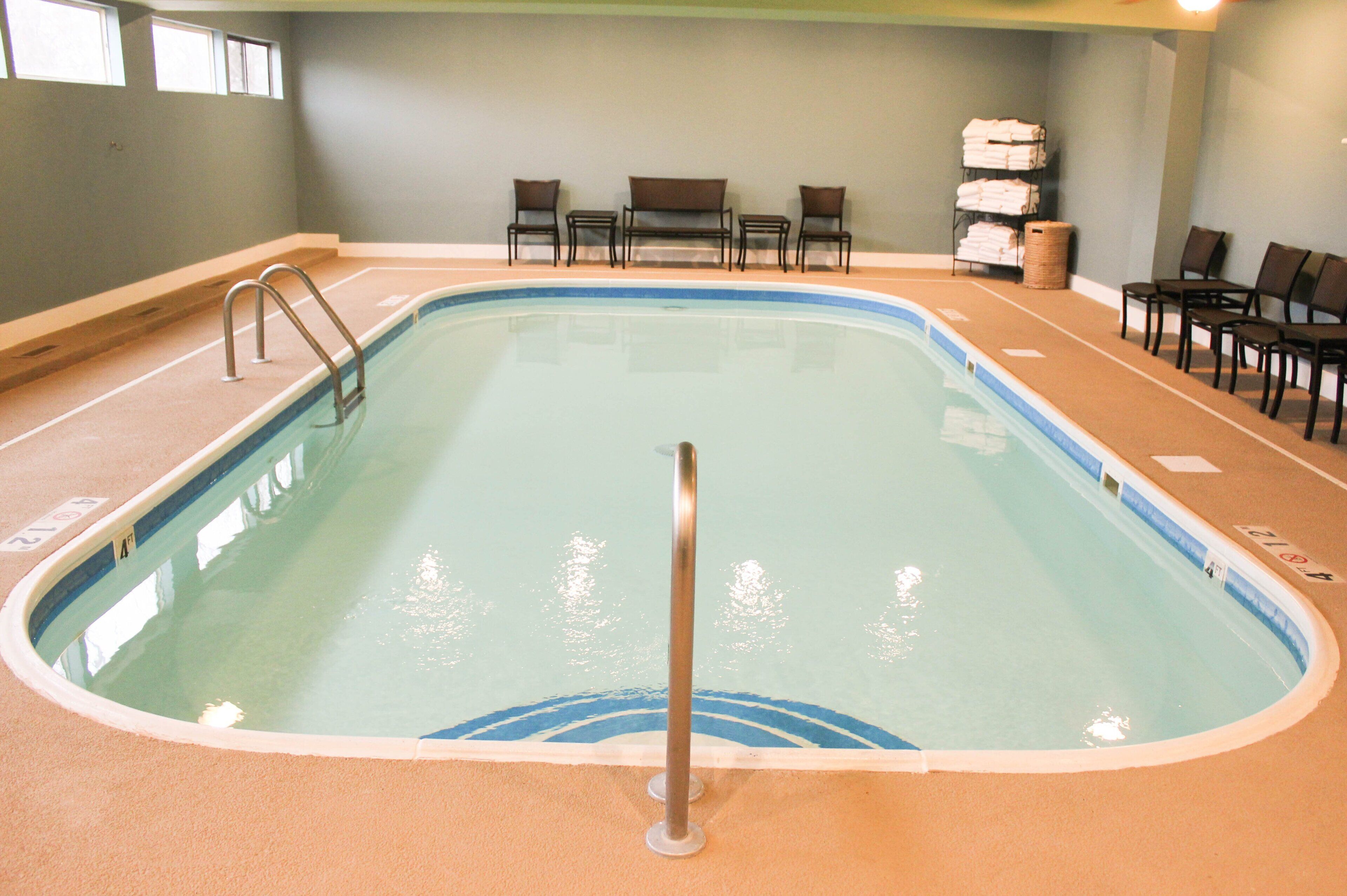 Una piscina interior con borde azul, una escalera de piscina y varias sillas alrededor del perímetro.