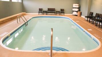 Una piscina interior con borde azul, una escalera de piscina y varias sillas alrededor del perímetro.