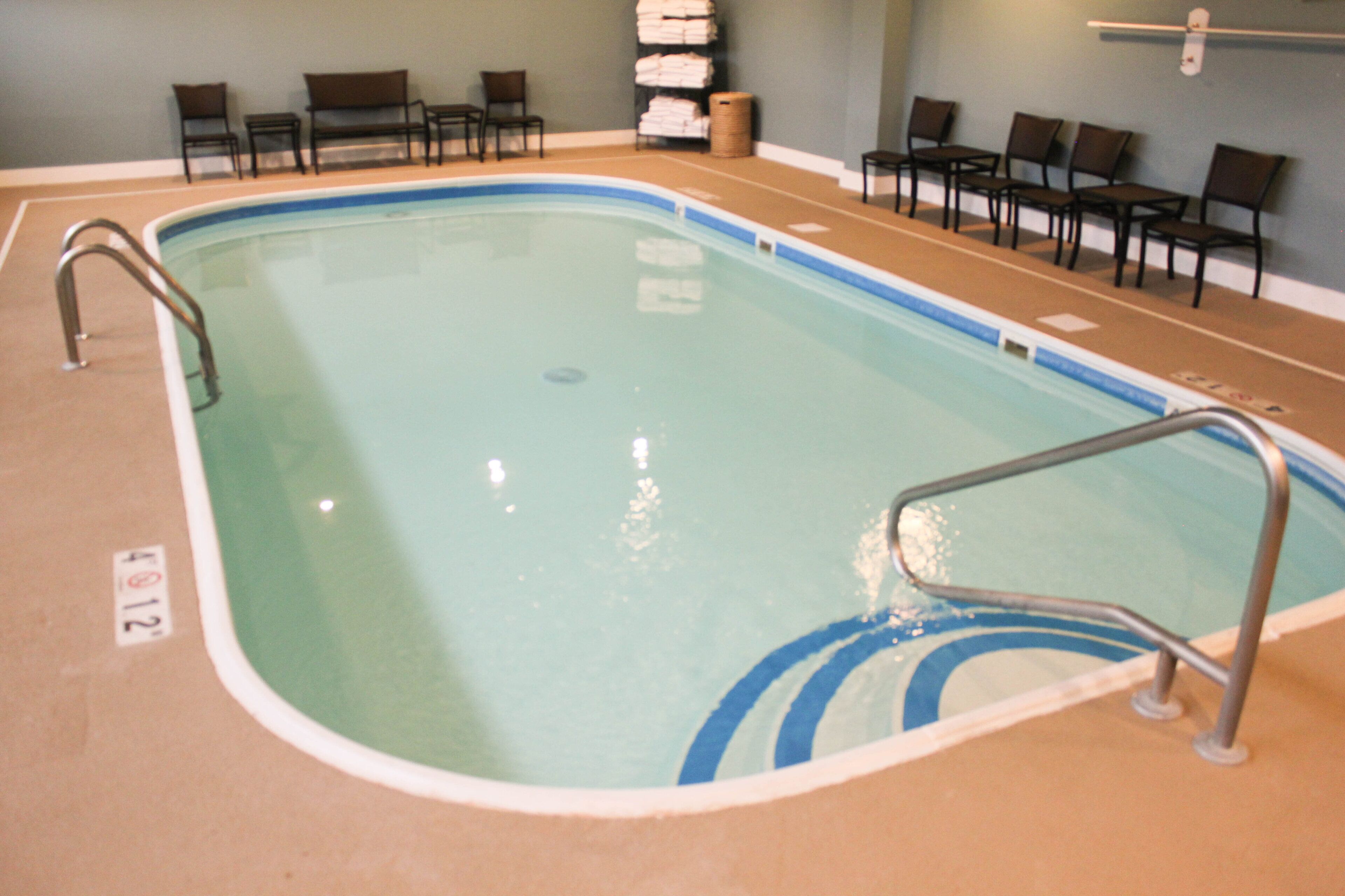 An indoor swimming pool with a metal ladder, chairs, and a towel rack.