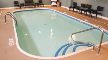 An indoor swimming pool with a metal ladder, chairs, and a towel rack.