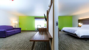 Een hotelkamer met een paarse bank, een houten bureau, een bed en een groene wand.