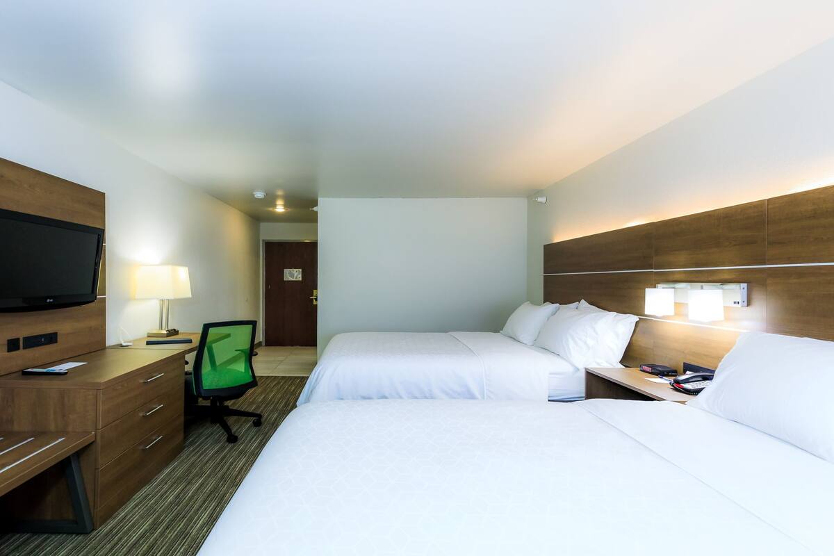 Ein Hotelzimmer mit zwei Betten, einem Schreibtisch, einem Flachbildfernseher, einem Sessel und einer Lampe.