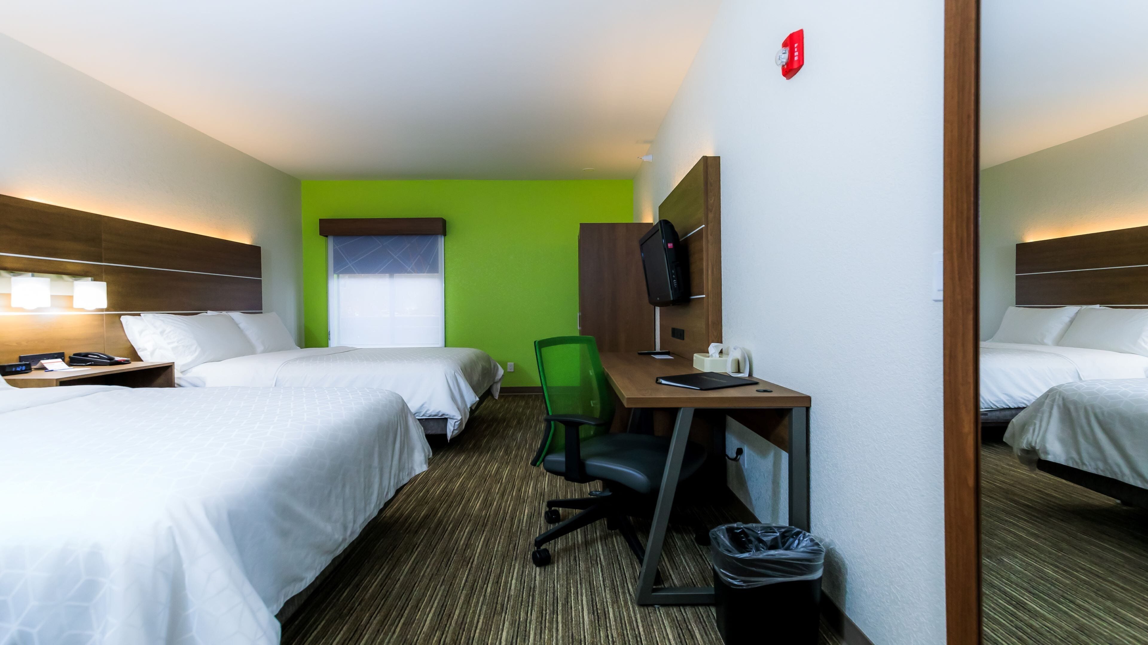 A hotel room with two beds, a desk, a chair, a TV, and a trash bin.