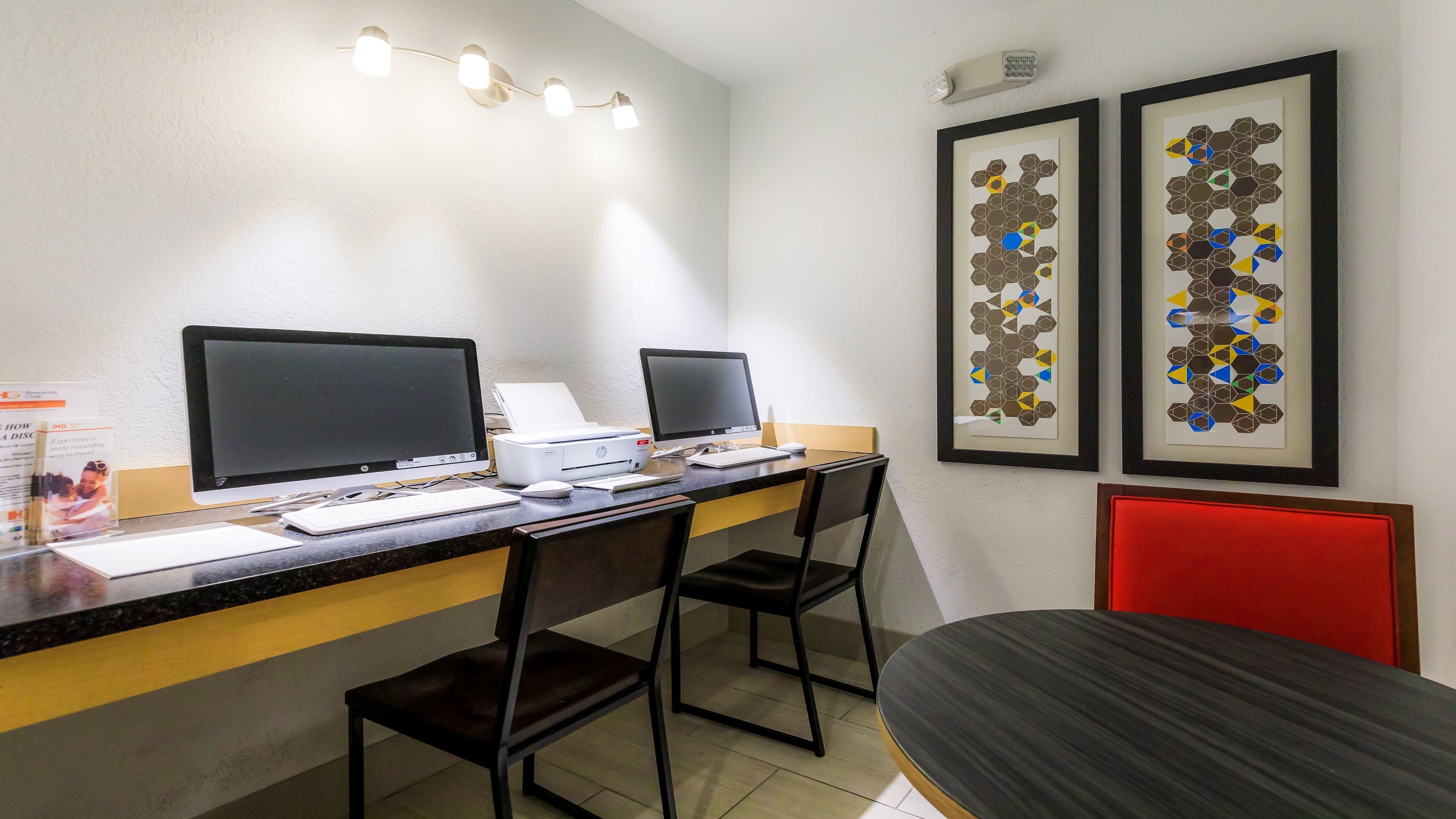 A workspace with two desktop computers, a printer, and framed artwork on the wall.