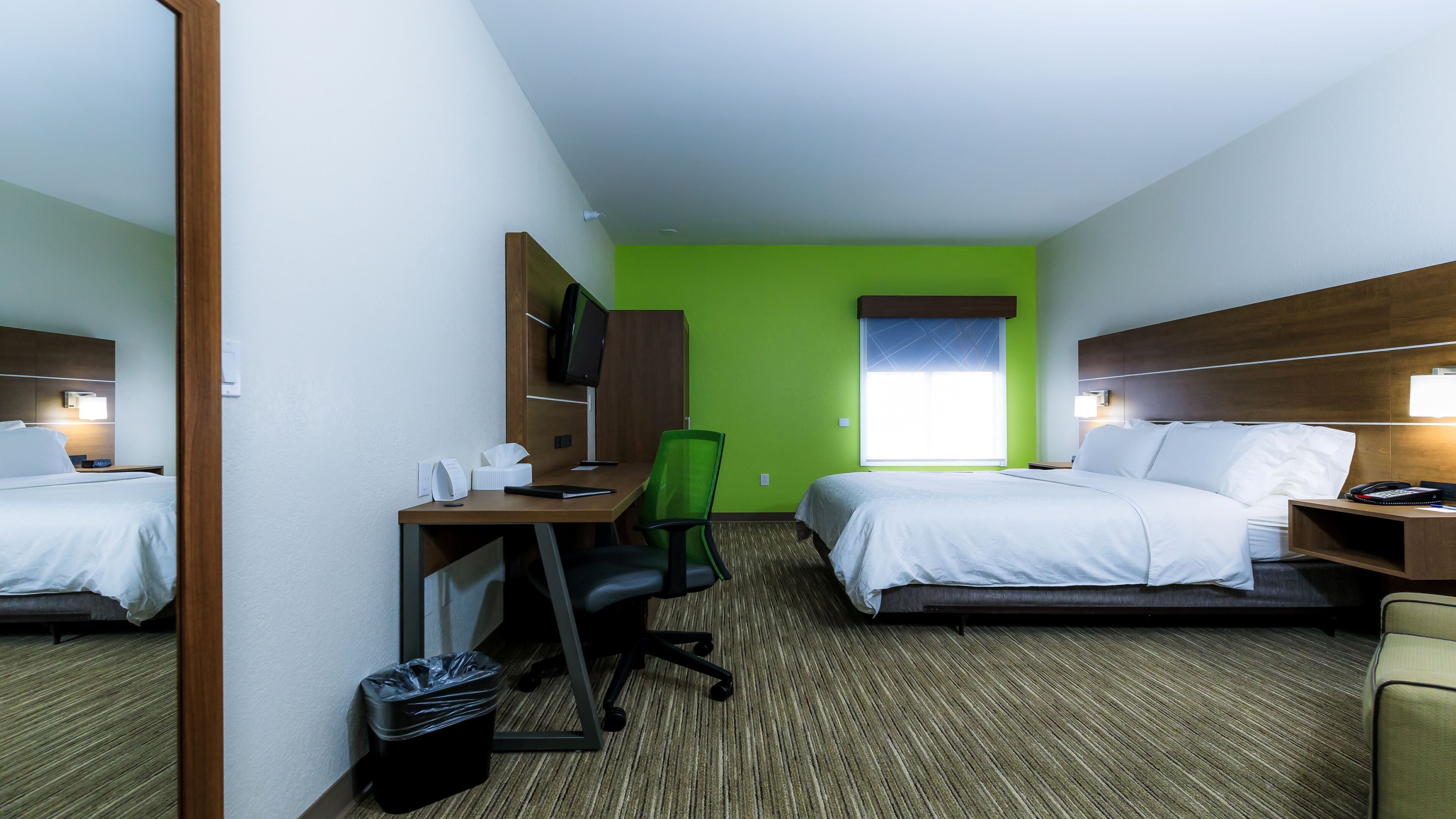 A hotel room with two beds, a desk, a chair, a TV, and a window.