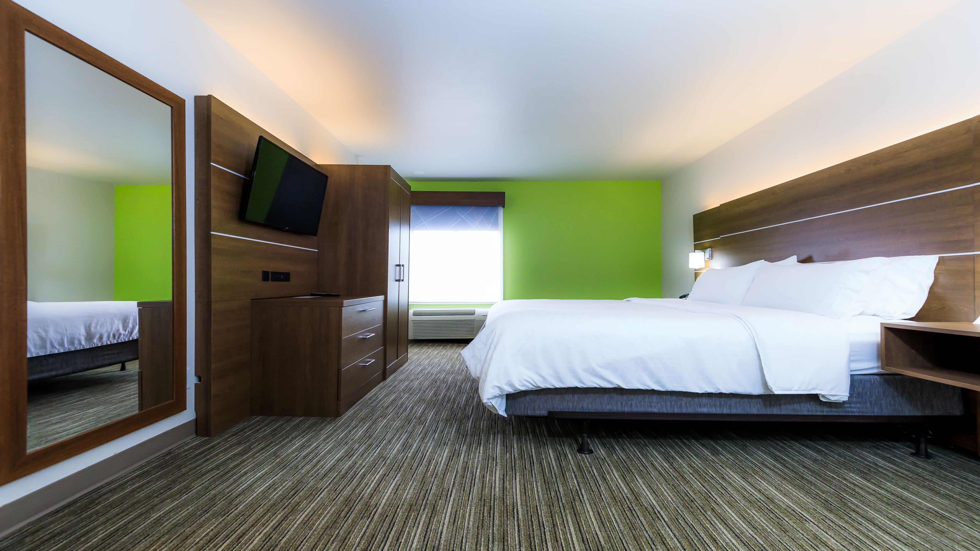 A hotel room with a bed, a desk, a chair, a mirror, and a television.