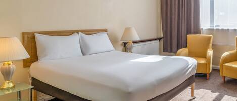 Un lit bien fait, avec du linge de lit blanc, une lampe de chevet, une chaise et une fenêtre avec des rideaux.