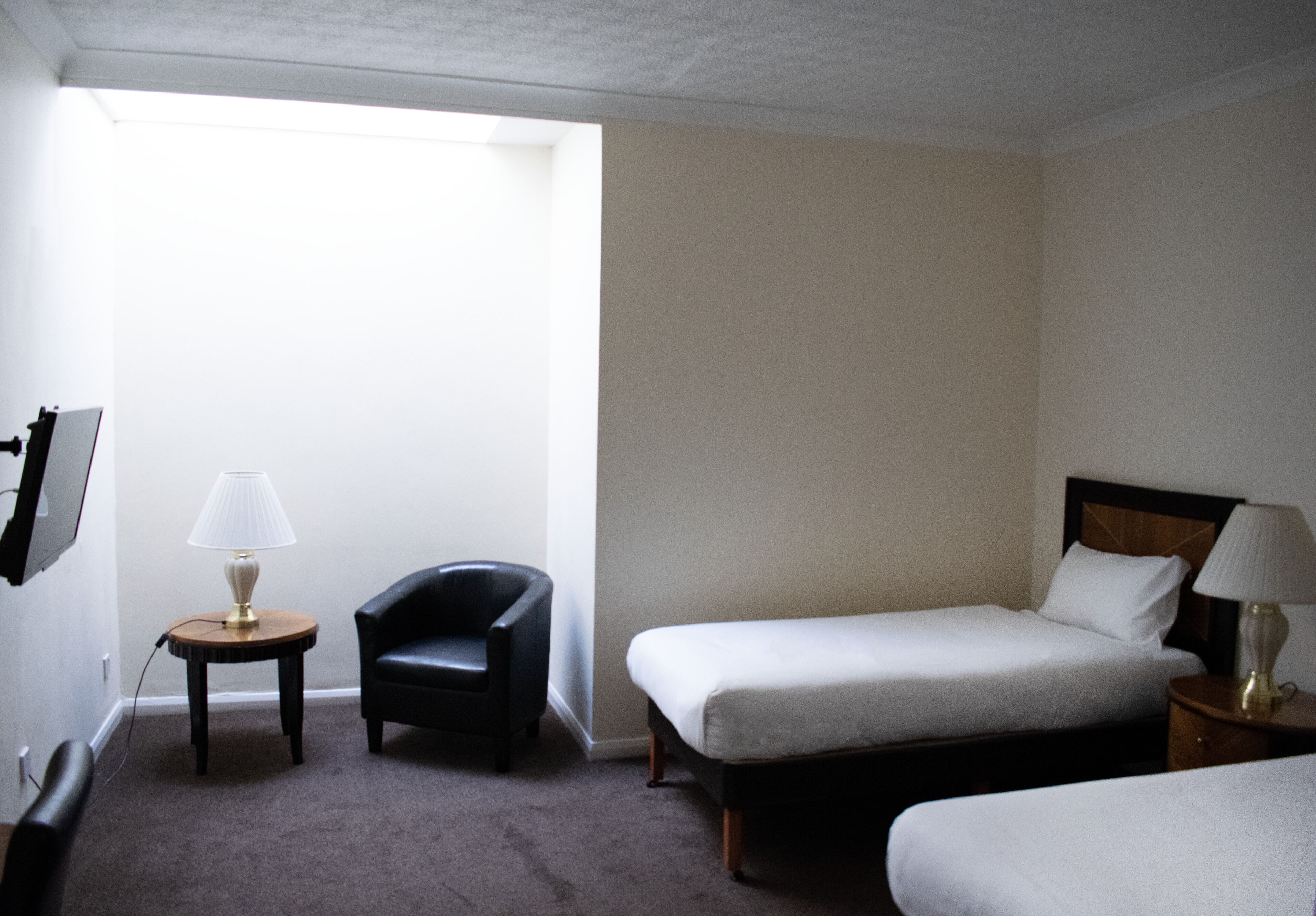 A hotel room with two beds, a chair, a small table, and a lamp.