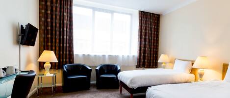 A hotel room with two beds, a desk with a computer, two chairs, and a TV on the wall.