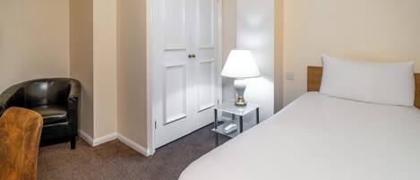A hotel room with a bed, a chair, a lamp, and a wardrobe.