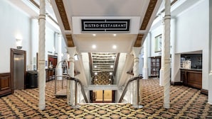 A grand lobby with a 'BISTRO-RESTAURANT' sign, ornate columns, a patterned carpet, and a staircase leading to an upper level.