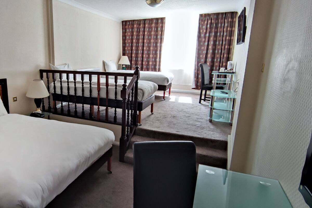 Quarto de hotel com uma cama grande, uma escrivaninha, uma cadeira e uma pequena mesa.