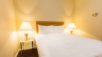Una habitación de hotel con una cama, dos lámparas de noche y una mesita pequeña.