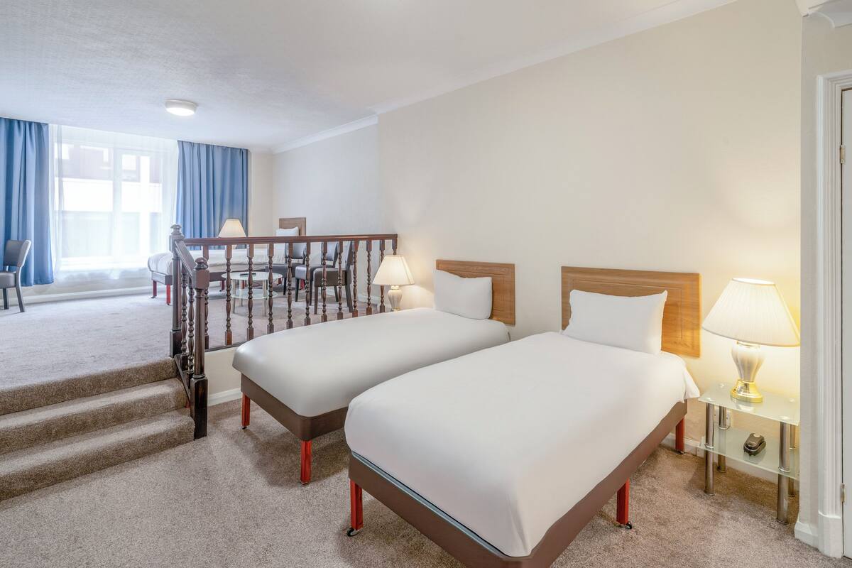 Quarto de hotel com duas camas, uma escada, uma escrivaninha e uma cadeira.